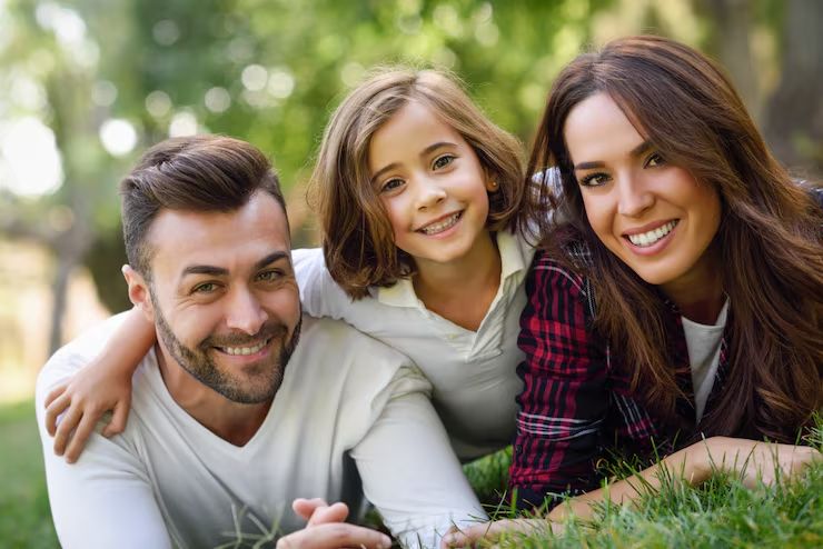 Casal e filha deitados na grama sorrindo